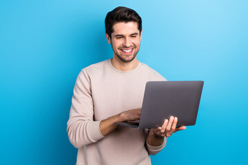 Canvas Print - Portrait of satisfied pleasant guy with brunet hair wear light pullover look at laptop typing message isolated on blue color background