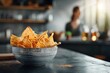 Close-up of crispy tortilla chips in a bowl, blurred background of a kitchen.