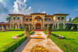 Opulent residence facade with vibrant lawn and decorative pathway to a grand porch entrance, showcasing luxury living.