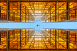 Looking up a golden symmetrical skyscraper to an flying aircraft in the very blue sky