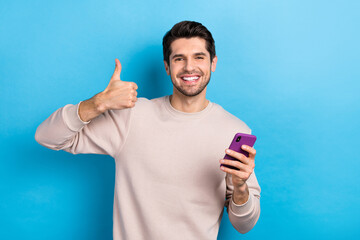 Poster - Photo of cheerful man with stylish haircut dressed beige sweatshirt hold smartphone showing thumb up isolated on blue color background