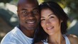 An adorable mixed-race couple embraces, smiles, and looks at the camera in this portrait.