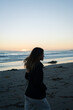 © Adrian Rodd/Stocksy - A young woman walks alone on the sandy shore of the beach
