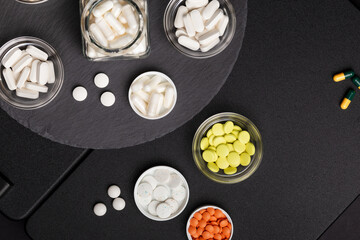 Wall Mural - Various vitamins, minerals and dietary supplements in jars from above on a black stone desk on a black background. Pills, tablets and capsules flat lay. Healthy lifestyle.