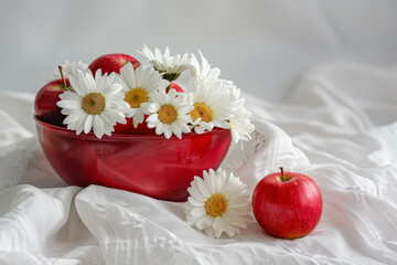 Wall Mural - A composition of white daisies and red apples, placed in a red bowl on a white tablecloth.