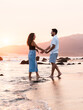 © Raul Navarro/Stocksy - Romantic young couple walking on the beach at sunset, holding hands