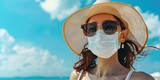 Fototapeta Londyn - Woman wearing a mask on the beach while traveling on vacation to help prevent the spread of diseases to immunocompromised people