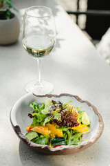 salad in a beautiful kitchen utensil and a glass of white wine outdoors on a white table