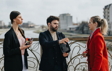 Sticker - Three young professionals engage in a serious discussion during an outdoor business meeting with a river backdrop.