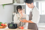 Fototapeta  - スマホを見ながらキッチンで料理を作る夫婦（レシピサイト・レシピアプリ）
