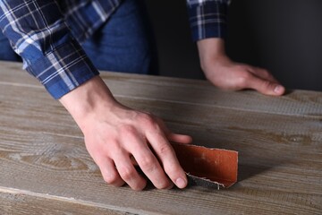 Man polishing wooden table with sandpaper, closeup