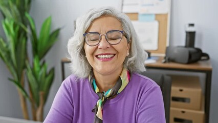 Sticker - Smiling woman with glasses and grey hair posing in an office environment, symbolizing professionalism and experience.