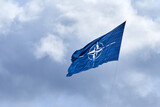 Fototapeta Tulipany - NATO flag on cloudy sky. Flying in the sky