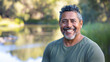 © Keitma - Latino american man in his 50s who exudes happiness and a sense of feeling truly alive in a beautiful natural park near lake, genuine smile on his face, relaxed and confident latin male who found joy