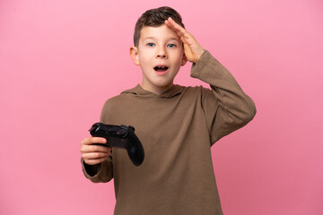 Wall Mural - Little caucasian boy playing with a video game controller isolated on pink background with surprise expression