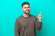 Young caucasian man isolated on blue background showing and lifting a finger in sign of the best