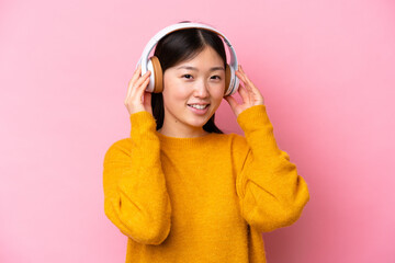 Wall Mural - Young Chinese woman isolated on pink background listening music