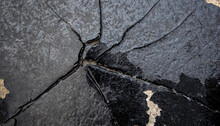 A Close-up Black And White Shot Of A Cracked Wall Showing Signs Of Deterioration And Wear. The Cracks Cut Through The Concrete Surface, Creating A Striking Contrast Between The Dark Shadows And Light