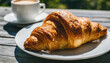 A typical French croissant, freshly baked with a cup of coffee in the background.