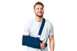 Young caucasian man with broken arm and wearing a sling over isolated chroma key background thinking an idea while looking up