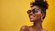 A stylish young woman with a radiant smile, wearing trendy sunglasses, standing against a sunny yellow background
