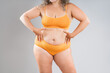 Fat woman in orange underwear on gray background, obesity and cellulite, overweight female body, weight loss concept