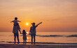 © Garun Studios - together, sun, sunset, sunrise, relaxation, parent, freedom, silhouette, son, beach. A family is standing on the beach, with the sun setting in the background. children are holding hands with parents.