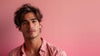 Young man with tousled hair looking at the camera against a pink background, wearing a casually unbuttoned shirt exuding confidence and a relaxed demeanor.