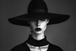 A monochrome image of a fashion model in sophisticated black attire with a wide-brimmed hat