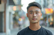 Young Asian Man in Urban Setting Portrait. Close-up of a young Asian man's face with a blurred city street background, looking directly at the camera.