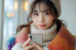 A cozy portrait of a young woman wrapped in a vibrant multicolored scarf and wearing a warm hat holding a phone