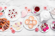 Mother's Day tea table scene over a white wood background. Variety of sweet desserts and pastries.