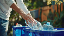 A Person's Hand Is Placing A Clear Plastic Bottle Into A Recycling Bin.