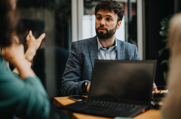 Wall Mural - Two business partners discussing over a laptop in a modern office setup, showcasing teamwork and collaboration.