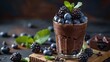 a glass of chocolate pudding with blueberries and blackberries on a wooden board against a dark background with a low angle