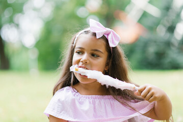 Wall Mural - Child girl eats cotton candy on a sunny summer day. Walk with children in the park on vacation.