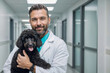 Man veterinarian is holding a black poodle dog in the hallway of the veterinary clinic and smiling