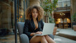 Gorgeous and sexy african-american lady, businesswoman in erotic attire sitting on an armchair with her laptop. Her expression reflects focus as she works attentively on the computer screen