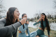 © qunica.com - Three joyful female friends in sportswear enjoying a light-hearted moment together by the lakeside park.