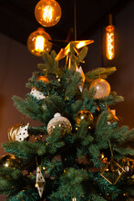 Modern Christmas Tree With Warm Edison Bulb Lighting. A Festive Christmas Tree Adorned With Gold And White Ornaments, Complemented By Stylish Edison Bulb Lights.