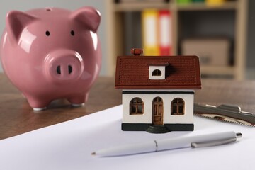 Wall Mural - House model, piggy bank, clipboard and pen on wooden table indoors