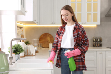 Canvas Print - Woman with spray bottle and microfiber cloth cleaning sink in kitchen