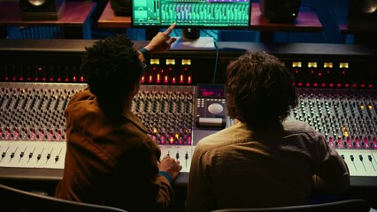 Poster - Team of sound engineers working on recording and editing tracks in professional studio control room, collaborating on mix and master audio files. Musician and technician pressing sliders. Camera B.