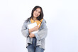 A smiling young Asian student wearing blue jacket yellow t-shirt while holding note books and looking at the camera, isolated by white background.