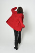 full length portrait of beautiful brunette woman model, wearing red trench coat jacket leather pants. standing pose in backview, walking away the camera. isolated silhouette on white studio background