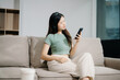 © Nuttapong punna - Young asian woman relax on comfortable couch at home texting messaging on smartphone and tablet smiling girl use cellphone  shopping online