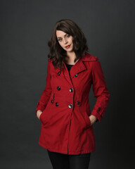 Wall Mural - close up portrait of beautiful brunette woman model, wearing red trench coat jacket with gestural hands posing.
isolated on dark studio background with shadows. 