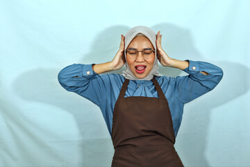 shocked screaming young housewife woman in hijab, glasses and brown apron closed eyes, covering ears with hands isolated on white background. People housewife muslim lifestyle concept
