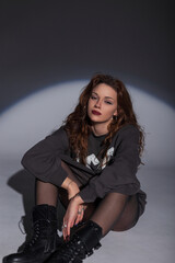 Canvas Print - Fashion girl in stylish clothes with a sweatshirt, tights and boots sits on the floor in the studio