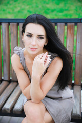 Wall Mural - Beautiful, young dark-haired girl in a summer dress sitting on a bench